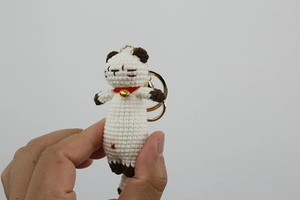 Detail of handmade crochet white kitten charm with brown ears and a golden bell