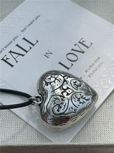 Macro shot of an antique silver heart pendant with floral carvings on black cord