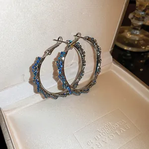 Detailed macro view of large silver twisted hoop earrings with blue pavé crystals in a box