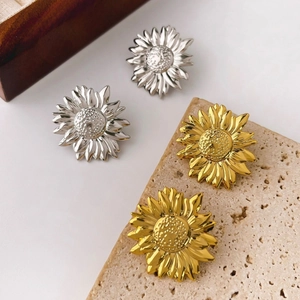 Elegant gold and silver sunflower stud earrings displayed on a white and wooden surface