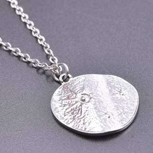 Detailed close-up of a silver stainless steel necklace featuring a textured sun pendant
