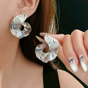 Detailed close-up of large silver earrings with unique spiral texture on model