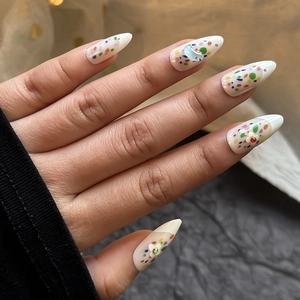 Detail of almond-shaped press-on nails with colorful dots and 3D floral accents