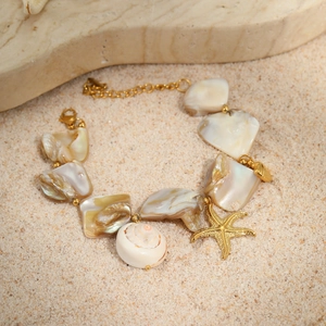 Detail of a gold ocean bracelet with shells, a conch, and a starfish on sand