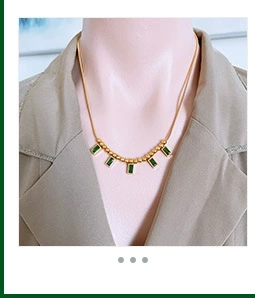 Detail of a double-layered gold snake chain with green rectangular pendant drop charms