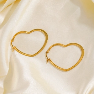Exaggerated gold stainless steel heart hoop earrings on beige silk fabric backdrop
