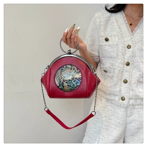 Detail of red shell bag featuring intricate elephant embossing and silver metal ring handle