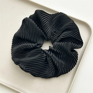 Detail of black pleated satin hair scrunchie with silky sheen on minimalist tray