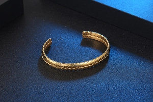 Detalle de brazalete abierto dorado con textura de espiga de trigo en metal pulido
