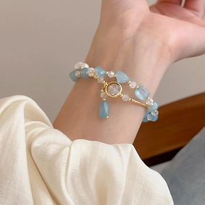 Dettaglio di un bracciale a doppio strato con pietre azzurre e perle bianche su un polso