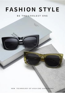 Top view of thick frame cat-eye sunglasses in shiny black and olive green on grey books