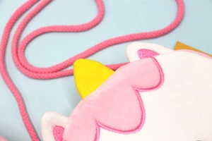 Détail du sac bandoulière licorne en peluche montrant la fourrure rose et la corne jaune