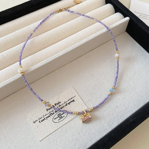 Detailed close-up of purple bead necklace with pearls and gold handbag pendant