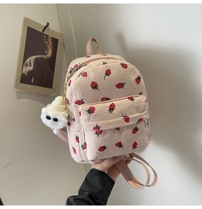 Detail of pink corduroy backpack with strawberry print and white plush charm pendant
