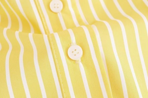 Detail of yellow and white striped shirt fabric with white four-hole buttons and fine stitching