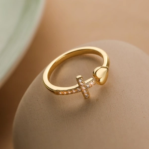 Close-up of gold-plated cross and heart ring with cubic zirconia on a smooth pebble
