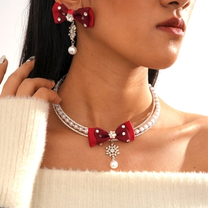 Detail of a Christmas necklace featuring a red bow, snowflake pendant, and double-row pearls