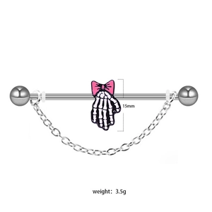 Industrial barbell piercing with silver skull hand, pink bow, and dangling chain details