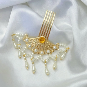 Goldener hohlgefächerter Haarkamm mit Perlen und Quasten auf weißem Seidenhintergrund