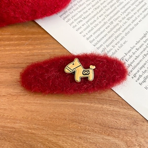 Macro detail of red plush hair clip with a golden pony ornament on a vintage wooden desk