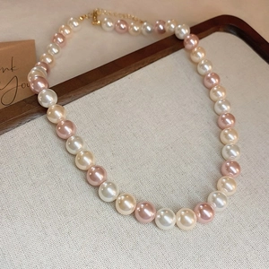 Detail of elegant white and pink pearl necklace with a gold clasp on textured fabric