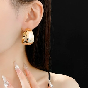 Close-up of golden chunky C-shaped hoop earrings with a textured hammered finish on model