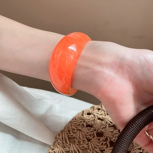 Detail of bright orange resin wide bangle with translucent cloud texture on a female wrist