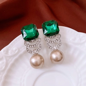 Detailed close-up of vintage style square green gem and pearl pendant earrings on a white plate