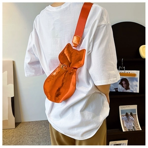 Detail of orange patent leather cat-shaped crossbody bag with metallic sheen and wide strap