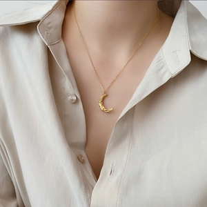 Detail of a golden crescent moon necklace with hammered texture worn by a model