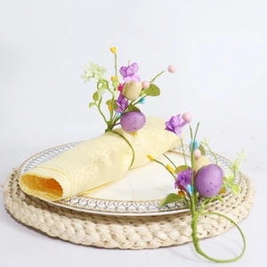 Detailed view of Easter napkin ring with purple eggs, artificial flowers and green leaves