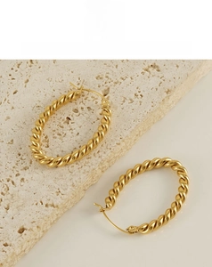 Detailed close-up of golden oval twisted hoop earrings on a marble stone base