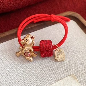 Détail d'un élastique à cheveux rouge avec pendentif cheval doré et cube de strass rouge