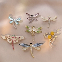 Detailed arrangement of seven dragonfly brooches with crystals and pearls on beige silk fabric