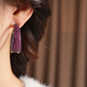 Close-up of large C-shaped earrings with purple and blue crystals on a female model