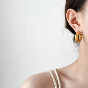 Close-up of chunky gold hoop earring showing polished finish and hollow oval C-shape
