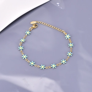 Détail du bracelet doré avec marguerites en émail bleu et étiquette en acier inoxydable