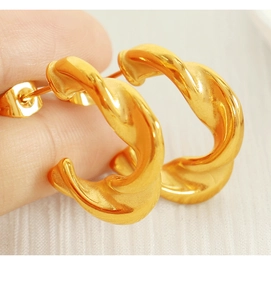 Close-up of gold twisted hoop earrings with a textured spiral design held by hand