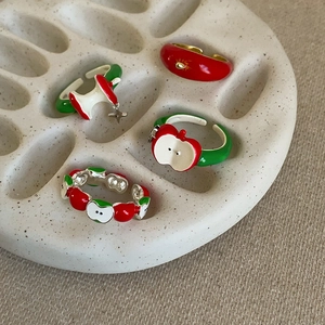 Close-up of apple-themed enamel rings in red and green on a ceramic display plate