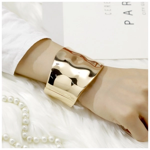 Detail of wide gold wavy cuff bracelet with polished finish worn on a wrist