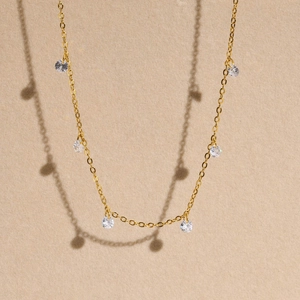 Elegant gold titanium steel necklace with small clear cubic zirconia charms on beige background