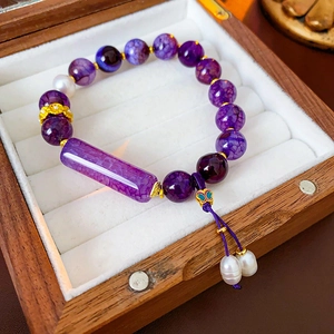 Close-up of purple agate beads, pearls, and enamel butterfly charm in a wooden jewelry box
