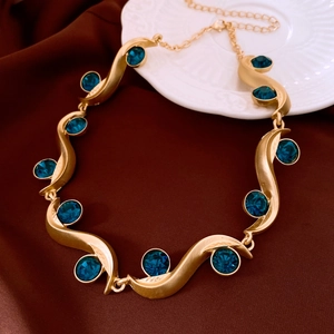 Detail of gold wavy necklace with deep blue rhinestones on dark silk fabric