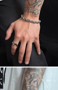 Close-up of men's chunky silver chain bracelet and wave ring on a tattooed arm