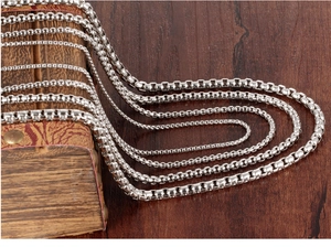 Multiple sizes of polished stainless steel box chains hanging on a rustic wooden stand