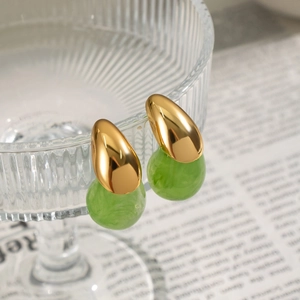 Close-up of gold water drop earrings with green jade texture pendants on newspaper