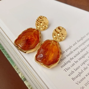 Gros plan de boucles d'oreilles ovales en résine ambre sur fond de livre ouvert