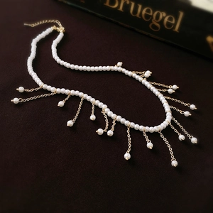 Elegant pearl choker necklace with gold fringe tassel on a dark luxury background
