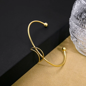 Detail of minimalist gold-plated open bangle with geometric ring and bead ends