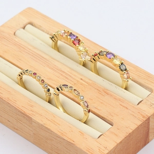 Primer plano de cuatro anillos dorados con circonitas de colores en un joyero de madera